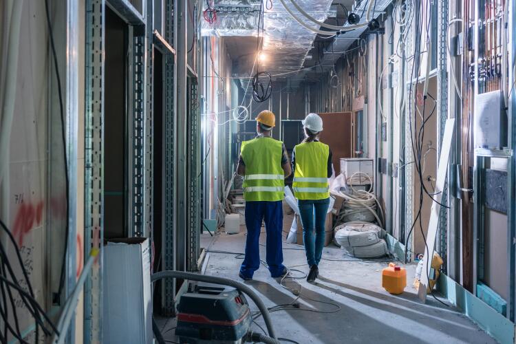 Two construction workers inspecting an indoor construction site. The site is equipped with electrical wiring and pipework, showcasing the use of Flowflex plumbing fittings and valves in the infrastructure.