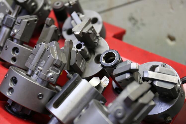 A collection of industrial tool holders and chucks, neatly arranged on a red surface. These precision tools are used in machining operations for securing and manipulating workpieces, highlighting the equipment involved in the Flowflex manufacturing process.