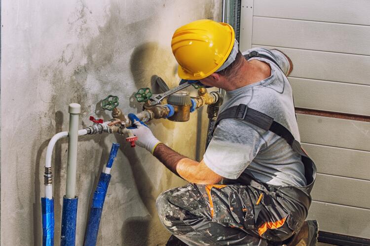 A plumber wearing a yellow hard hat and work clothes is adjusting pipes and valves on a residential plumbing system. This shows the use of Flowflex fittings and valves in residential applications, ensuring efficient and reliable water supply systems.