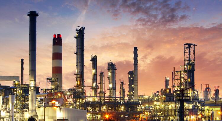 A large industrial facility with multiple towers and chimneys, illuminated at dusk. The complex infrastructure represents the use of Flowflex fittings and valves in the oil and gas industry for reliable performance in demanding environments.