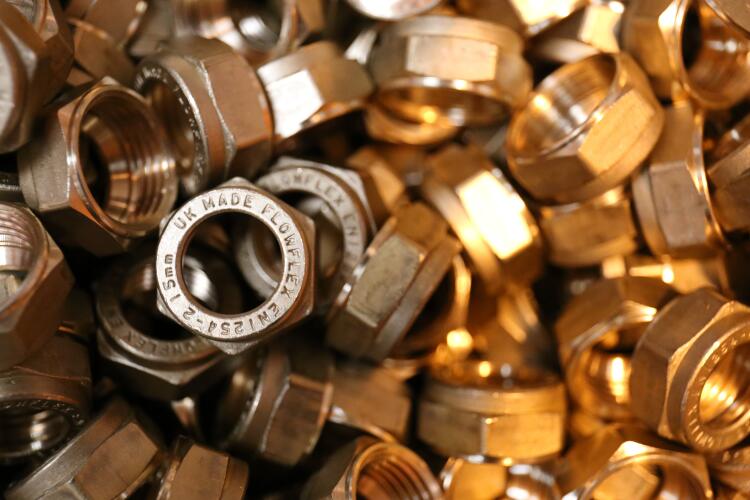 A pile of brass nuts stamped with “Flowflex UK Made,” showcasing Flowflex’s manufacturing of durable and reliable fittings for various applications.