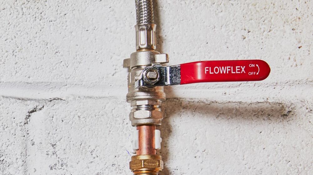 Flowflex ball valve on white wall connected to copper pipe and a flexible hose